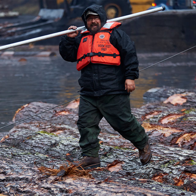 A man wearing Chippewa boots and standing on logs.